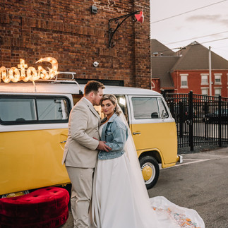 Bride and groom pose in front of a yellow vintage VW photo booth bus, Old Fashioned Photo BUs, during a wedding at Gibson Social Club in Oshkosh, WI