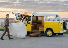 Bride and groom walk  into a vintage VW photo bus with colorful citrus-inspired florals and retro decor.