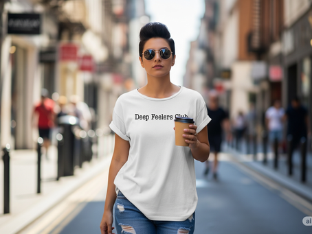 woman on walking down a city street wearing a white t-shrt with ripped jeans and sunglasses while holding a coffee. The shirt reads "Deep Feelers Club"