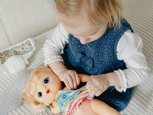 niña pequeña jugando a vestir a una muñeca