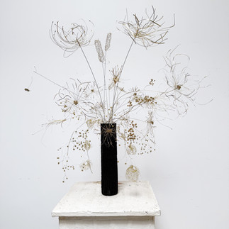 Plongez dans un jardin imaginaire avec cette sculpture florale unique, conçue sur un socle en béton brut, sculpté et peint à la main. L'artiste a adouci le matériau avec de l'encre acrylique, créant un contraste saisissant qui célèbre la beauté brute de la nature.  Cette œuvre d'art présente des roseaux sauvages élancés et des graminées délicates, qui côtoient de poétiques ailes d'ange. Des baies roses apportent de vives touches de couleur, tandis que la simplicité des pissenlits s'harmonise avec la complexité des dahlias.  Un détail fascinant insuffle un mouvement éternel à la pièce : une abeille figée en plein vol, sur le point de butiner une fleur des champs. Cette création artisanale, pièce unique de décoration murale, est une véritable célébration de la poésie de la nature.