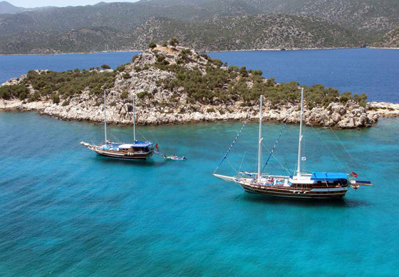 Two wooden yachts anchored at a rocky island in Kalkan.