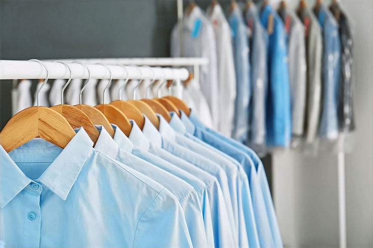 Portrait of ironed, blue men's shirts hanging on wooden hangers, front view.