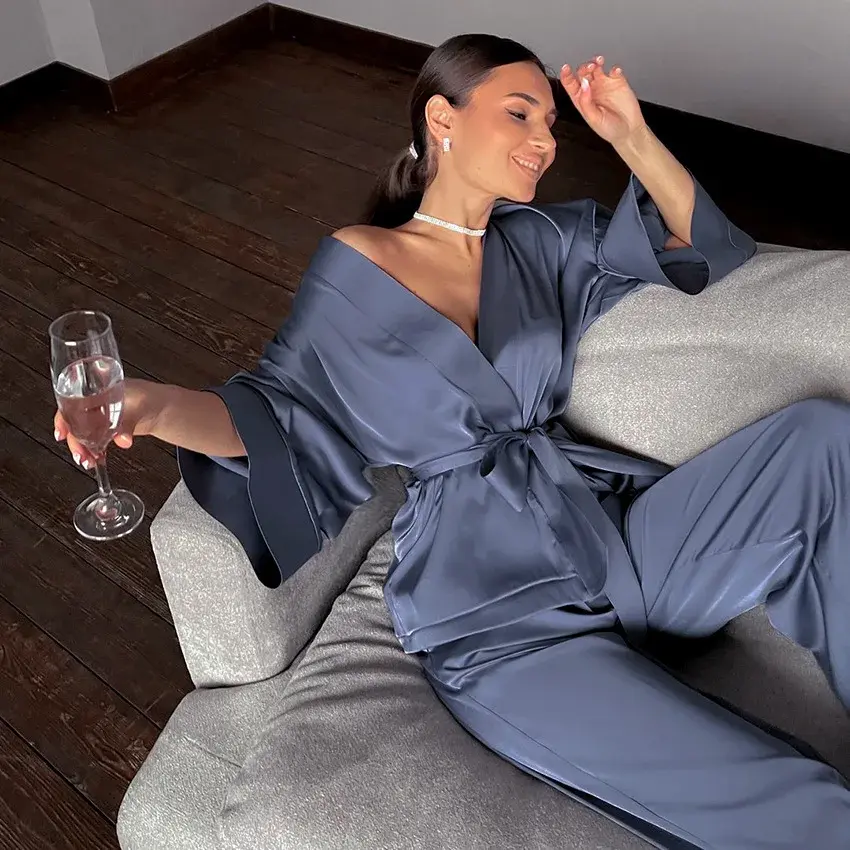 A smiling lady in pajamas sitting on a sofa and holding a worm containing wine.
