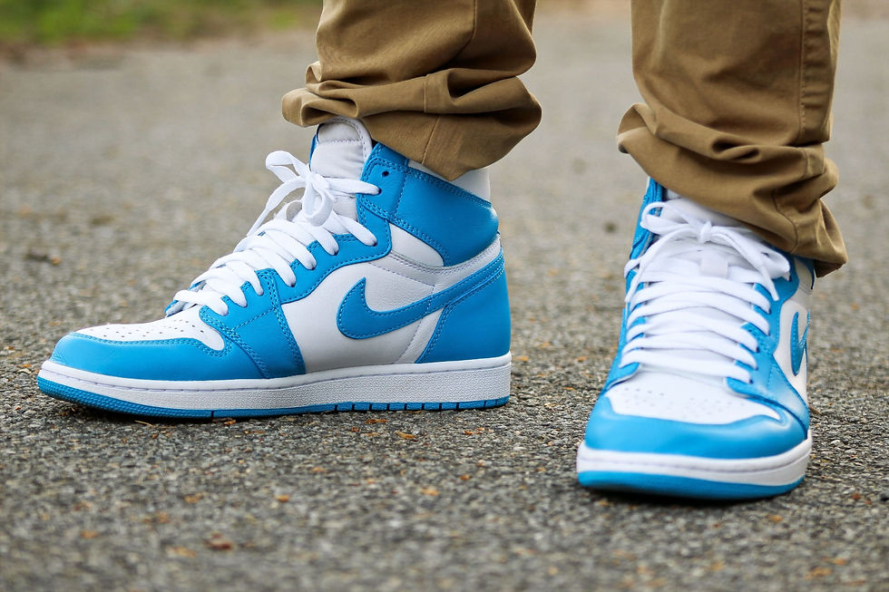 Portrait des pieds d'un homme portant des chaussures baskets, blanches/bleues et un pantalon brun, vue de face.