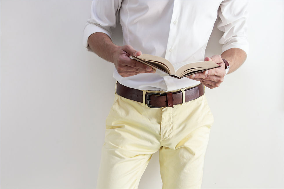 Portrait d'un homme portant un pantalon jaune, une chemise blanche, une ceinture marron, entrain de lire un bouquin, vue de face.