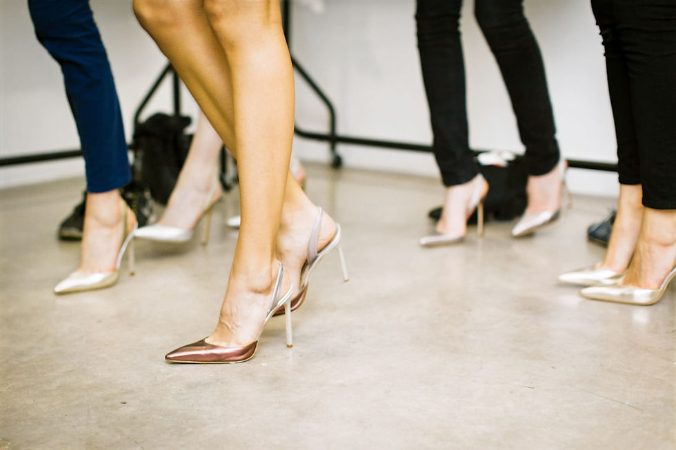 Portrait de cinq femmes portant des chaussures avec des talons hauts, différentes couleurs, se trouvant dans une salle, vue de face.