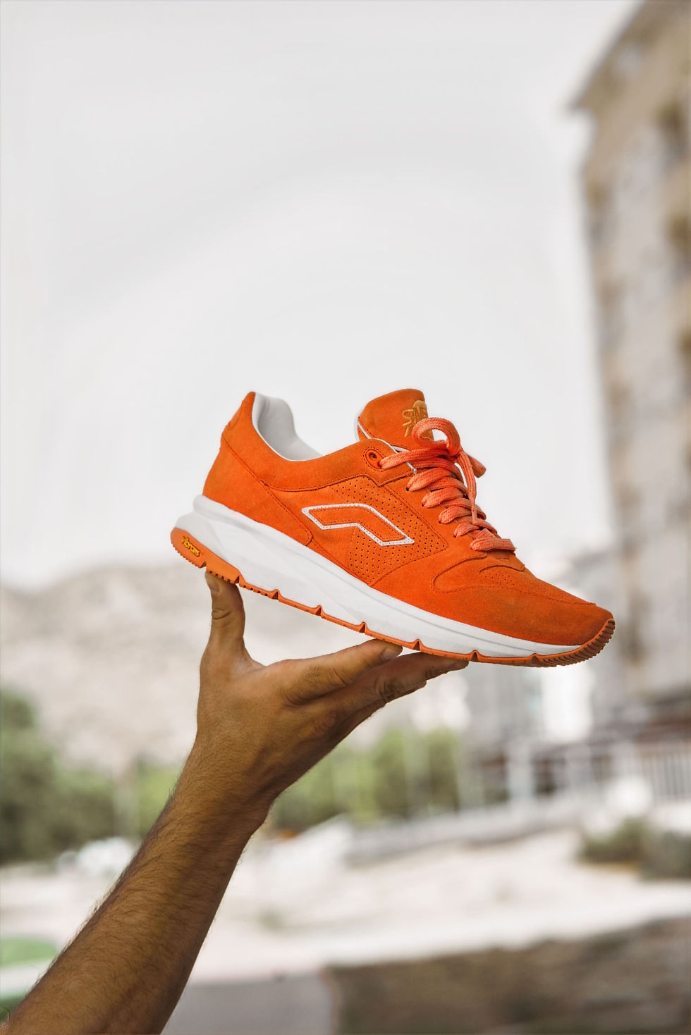 Portrait de la main d'un homme tenant une chaussure orange, vue de côté.