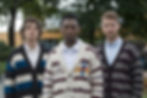 Portrait of 3 men wearing sweaters, striped, different colors, V-necks, front view.