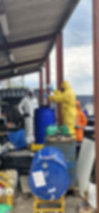 Operators wearing protective suits handling chemical materials around an industrial drum during a controlled training exercise