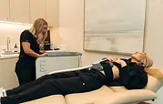 A patient lying on a treatment table with an Emsculpt Neo applicator on her abdomen at Thrive Medicine Clinic