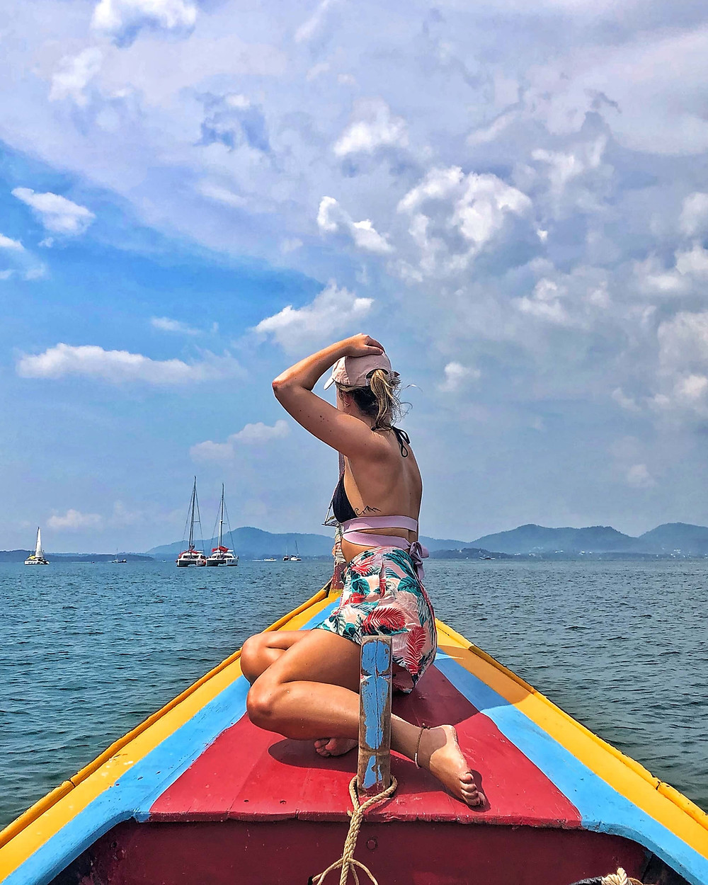 Girl on a colourful boat holding her hat with one arm