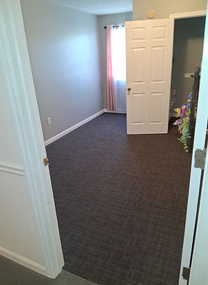 Bedroom with brown carpet, white door and window, and soft lighting.