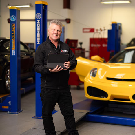 Automotive mentor standing beside yellow performance car in a workshop, photographed by Display in Christchurch NZ.