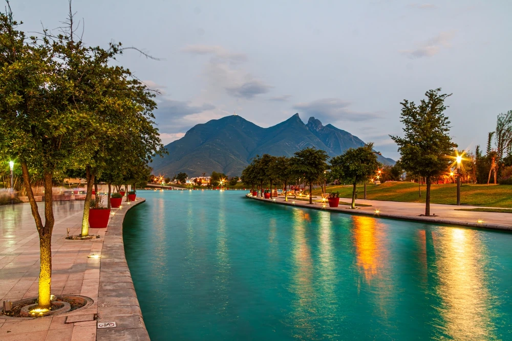 Illuminated lake at Macroplaza, with iconic Cerro de la Silla in the background. 