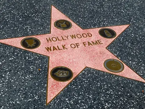 Estrella rosa del Hollywood Walk of Fame sobre acera negra, con texto visible y emblemas dorados.