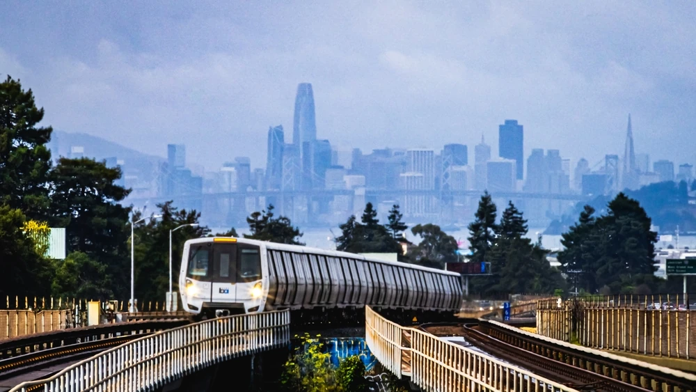 BART metro arriving at Rockridge station in Oakland CA, with skyline in the background.