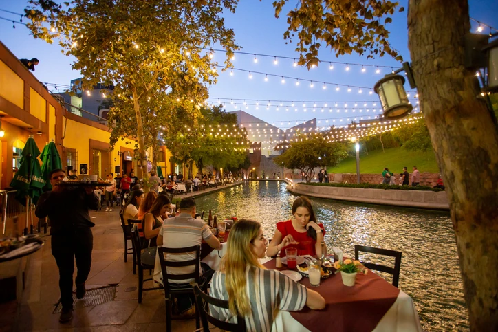 Turistas y locales disfrutan comidas en restaurantes del Paseo Santa Lucía al atardecer.