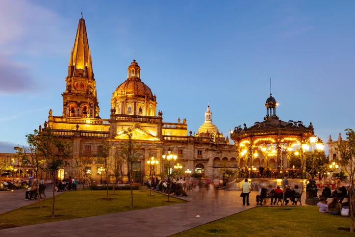 Catedral de Guadalajara y kiosco de Plaza de Armas iluminados al anochecer.