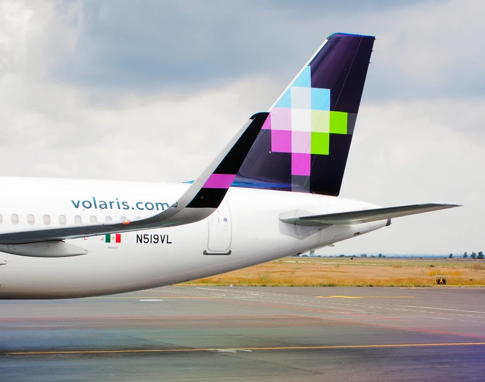 Avión de Volaris en pista, con el logo y el mensaje "100 aviones para que más personas viajen bien".
