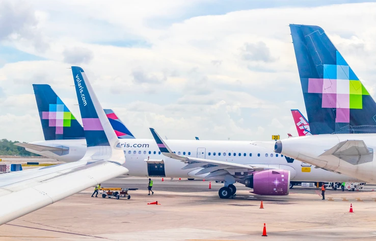 Avión de Volaris en pista, con el logo y el mensaje "100 aviones para que más personas viajen bien".