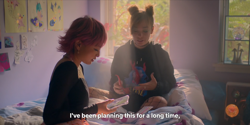 Quinni and Sasha are sitting on Quinni's bed. Sasha is on her phone. Quinni holds a headband with horns. Subtitle reads, "I've been planning this."