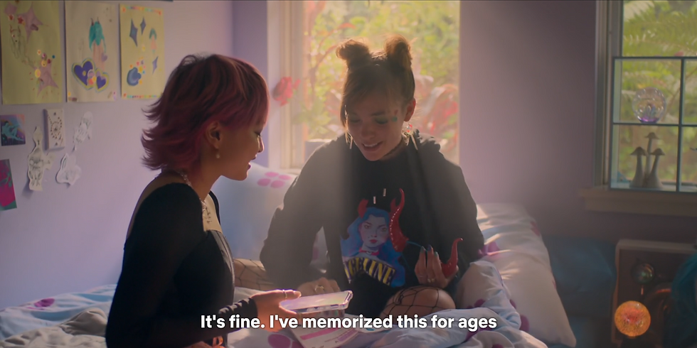 Sasha and Quinni sit on a bed in a colorful room with art on the walls. Sasha is holding her phone. Sunlight streams in. Quinni speaks excitedly. Caption reads: "It's fine. I've memorized this for ages."