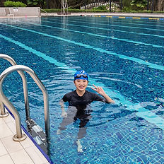 Child in swim cap and goggles smiling in pool, peace sign