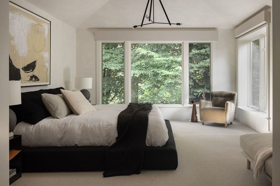 A modern bedroom with a black bed frame, neutral bedding, large windows, and a beige accent chair.