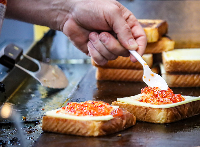 chef's hand using spoon to add hot pepper jam to grilled cheese sandwich
