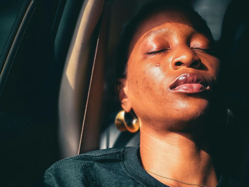 A woman of color, feeling exhausted leaning her head back onto the headrest in her car. 
