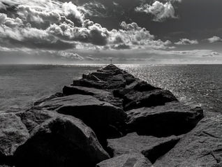 Black and white image of the Corona del Mar jetty with ocean and dramatic sky