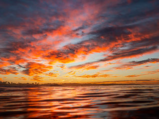 Fiery sunset sky over Newport Beach, reflecting across calm ocean waters in vivid orange and deep blue hues, captured from the water’s surface.