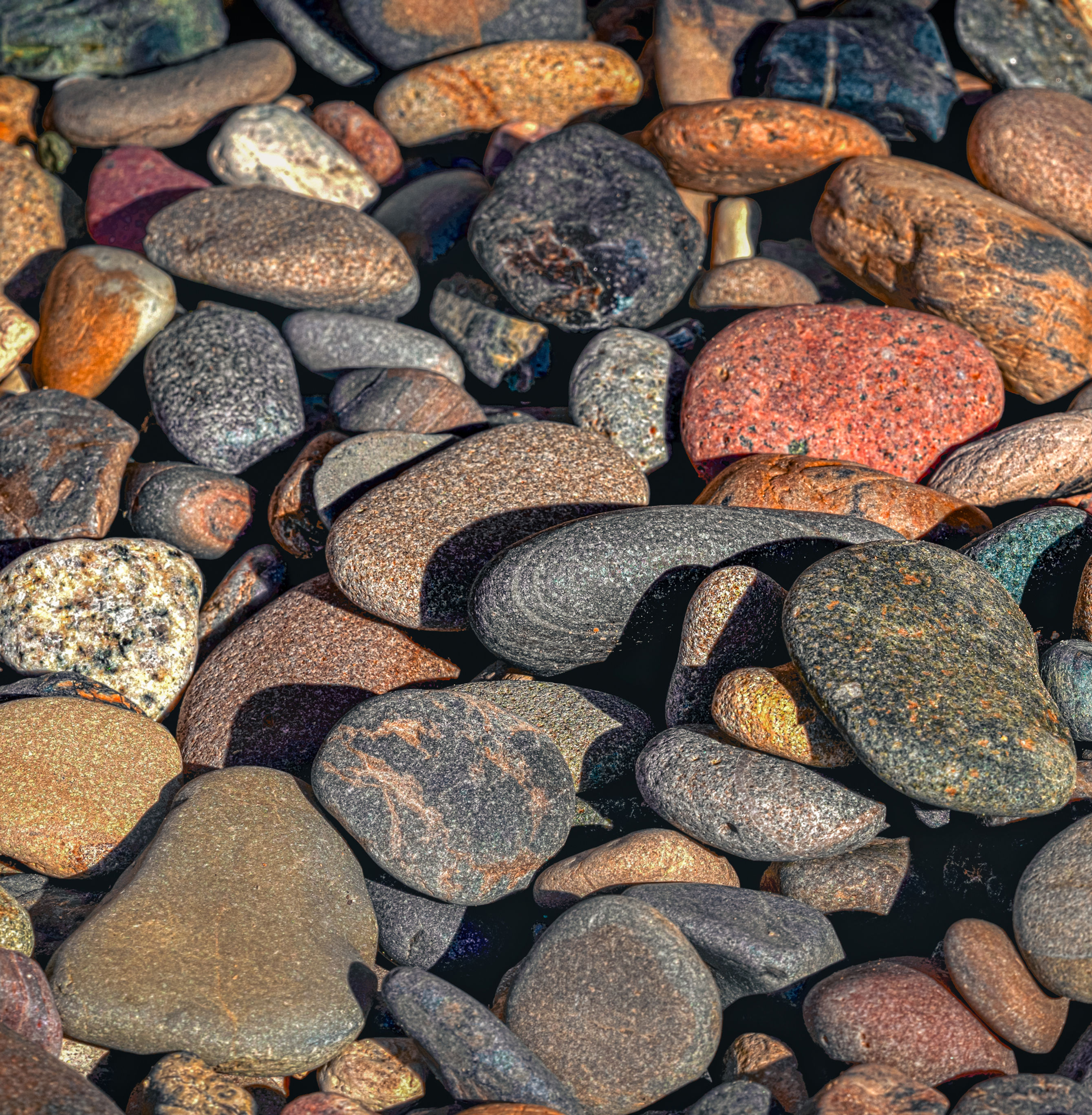 Abstract photo of smooth, multicolored sea stones underwater — a textured, meditative image in earthy coastal tones