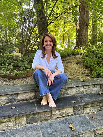 Deb Morgan, meditation and yoga teacher at Blissful Breath LLC, seated barefoot on stone garden steps surrounded by greenery radiating calm, approachability, and presence.