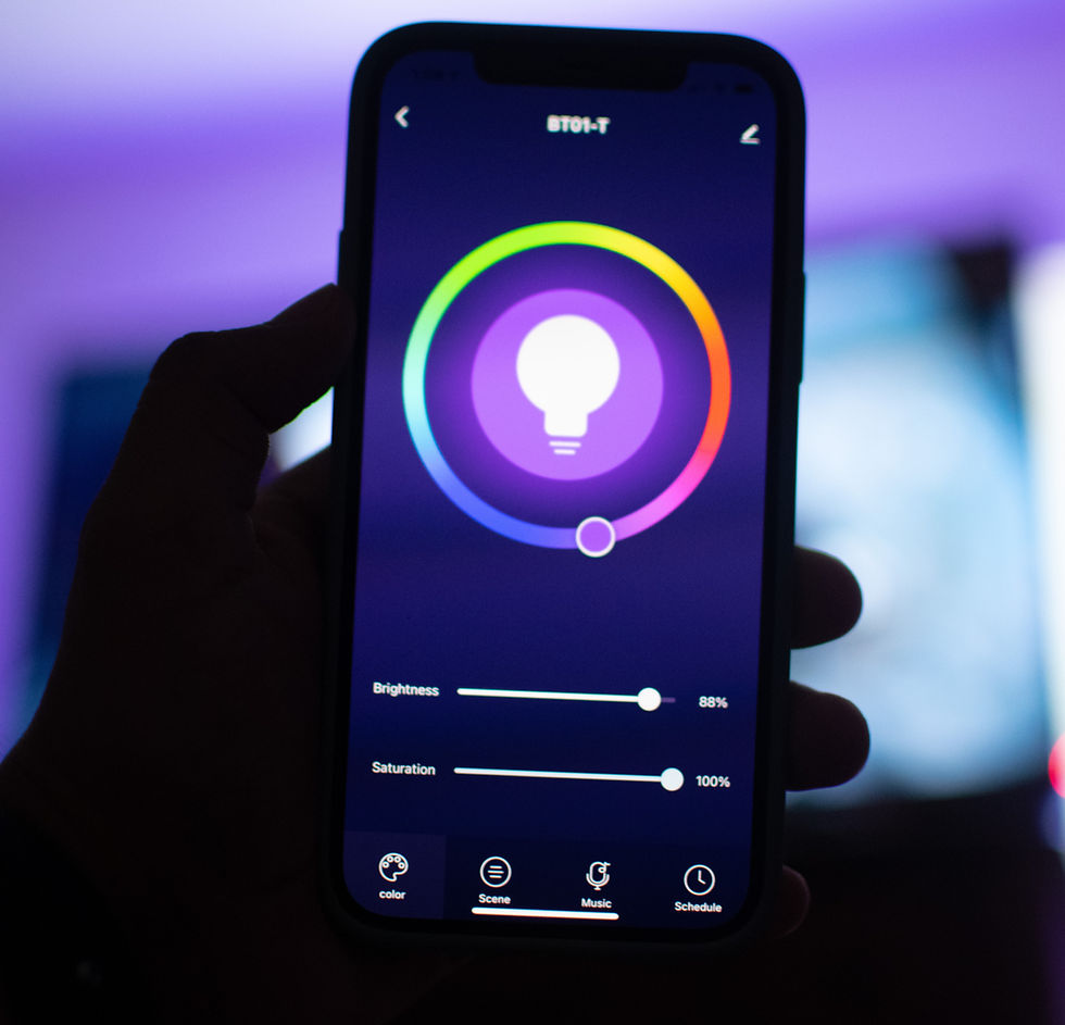 Hand holding a smartphone displaying a colorful lighting app interface. Background is softly blurred with purple hues.