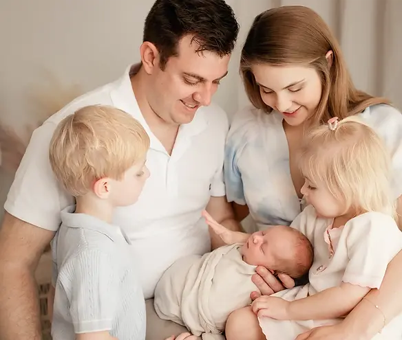 Mum and dad with three young children all gazing lovingly at their newborn baby during a studio newborn photography session in Brisbane with Natarsha March