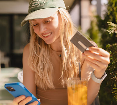 Happy young blonde woman with cap customer shopper holding credit card using cell phone mo
