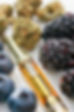 A vape cartridge full of cannabis oil surrounded by blackberries, blueberries, and dried cannabis flowers.