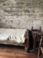 Rustic stone room with a wooden cradle and bed covered in a cream blanket. Warm, cozy atmosphere with wooden floors and walls.