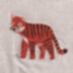 An embroidered tiger with big eyes and black stripes on orange fabric. Background is light-coloured, textured cloth.