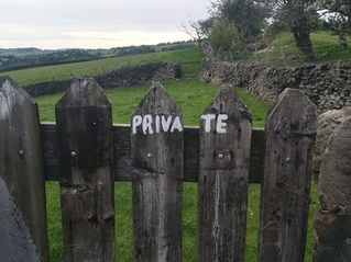 Weathered wooden fence with "PRIVATE" text, set in a green countryside with stone walls and trees under a cloudy sky.