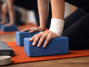 Close up of hands pressing into blue yoga blocks with a wrapped wrist during modified yoga practice at West Door Yoga in Bay Shore.