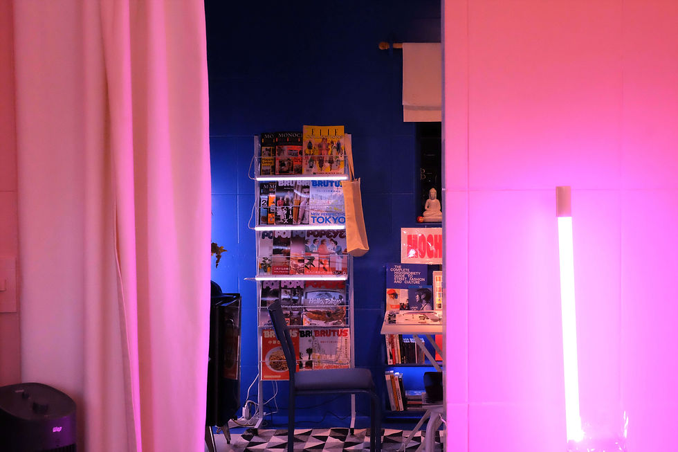 sala intimista iluminada por uma luz de neon pink e ao fundo vemos uma outra sala com revistas ao fundo