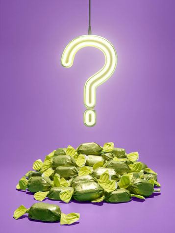 Quality Street photography – a glowing neon question mark hangs above a pile of green-wrapped Quality Street chocolates on a vibrant purple background, creating a playful and mysterious composition. Conceptual commercial food photography by advertising photographer Richard Jarrett, London.