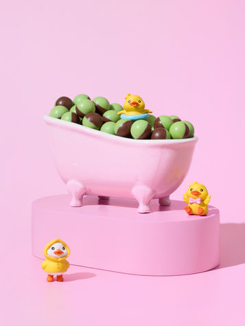 Surreal studio product shot of Nestlé Aero chocolate balls in a miniature pink bathtub with toy ducks. Playful, colourful still life concept by Richard Jarrett, London.