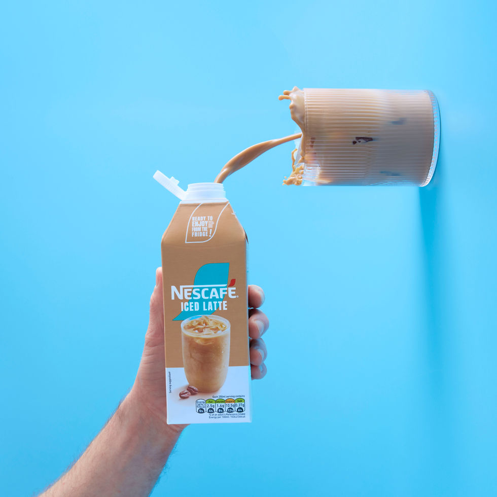 Beverage advertising photography showing Nescafé Iced Caramel Latte with a dramatic milk splash against a bright blue background.