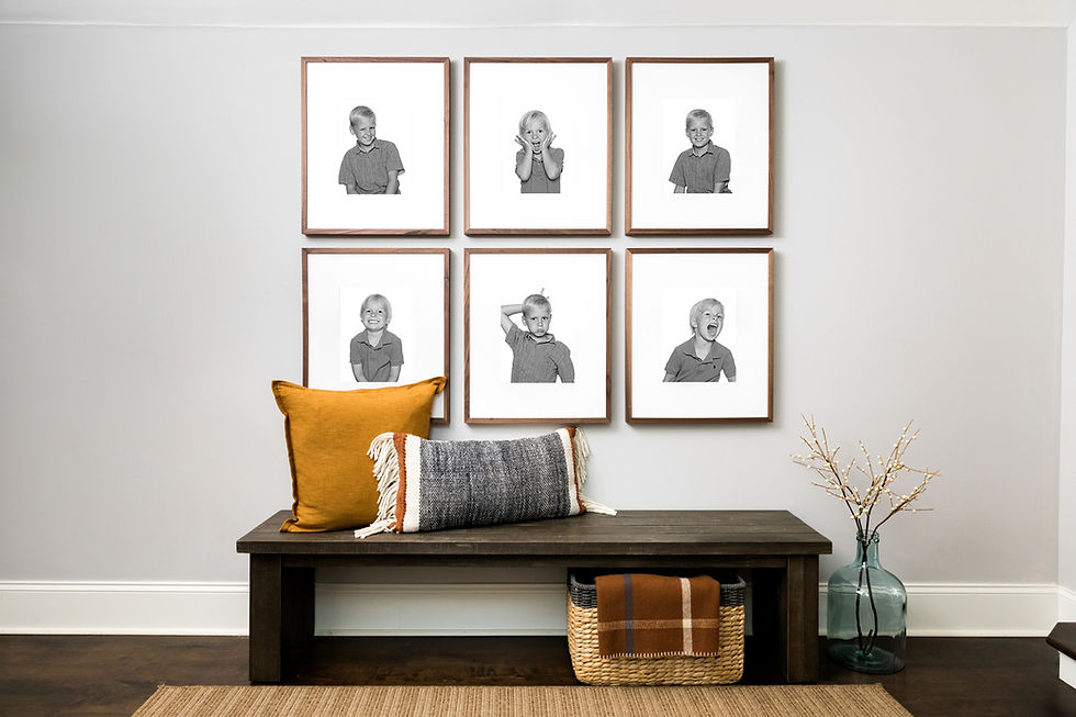 Six black-and-white portraits on a wall above a bench with yellow and gray pillows. A basket and vase are on the floor. Calm setting.