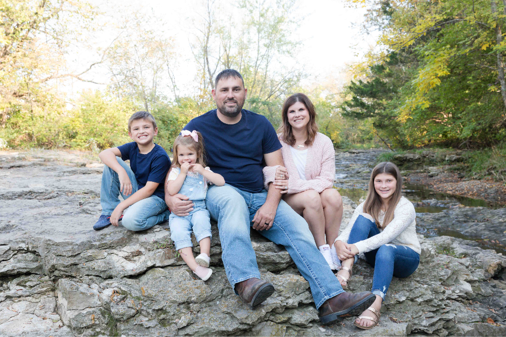 Family portrait: parents and three kids sitting on rocks by creek