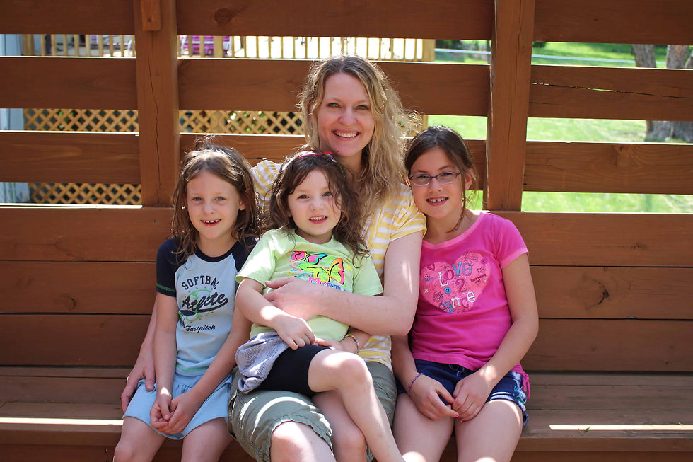 Woman with three smiling children on a wooden bench outdoors. Bright clothing: yellow, green, pink. Text: "Softball Athlete," "Love Dance."